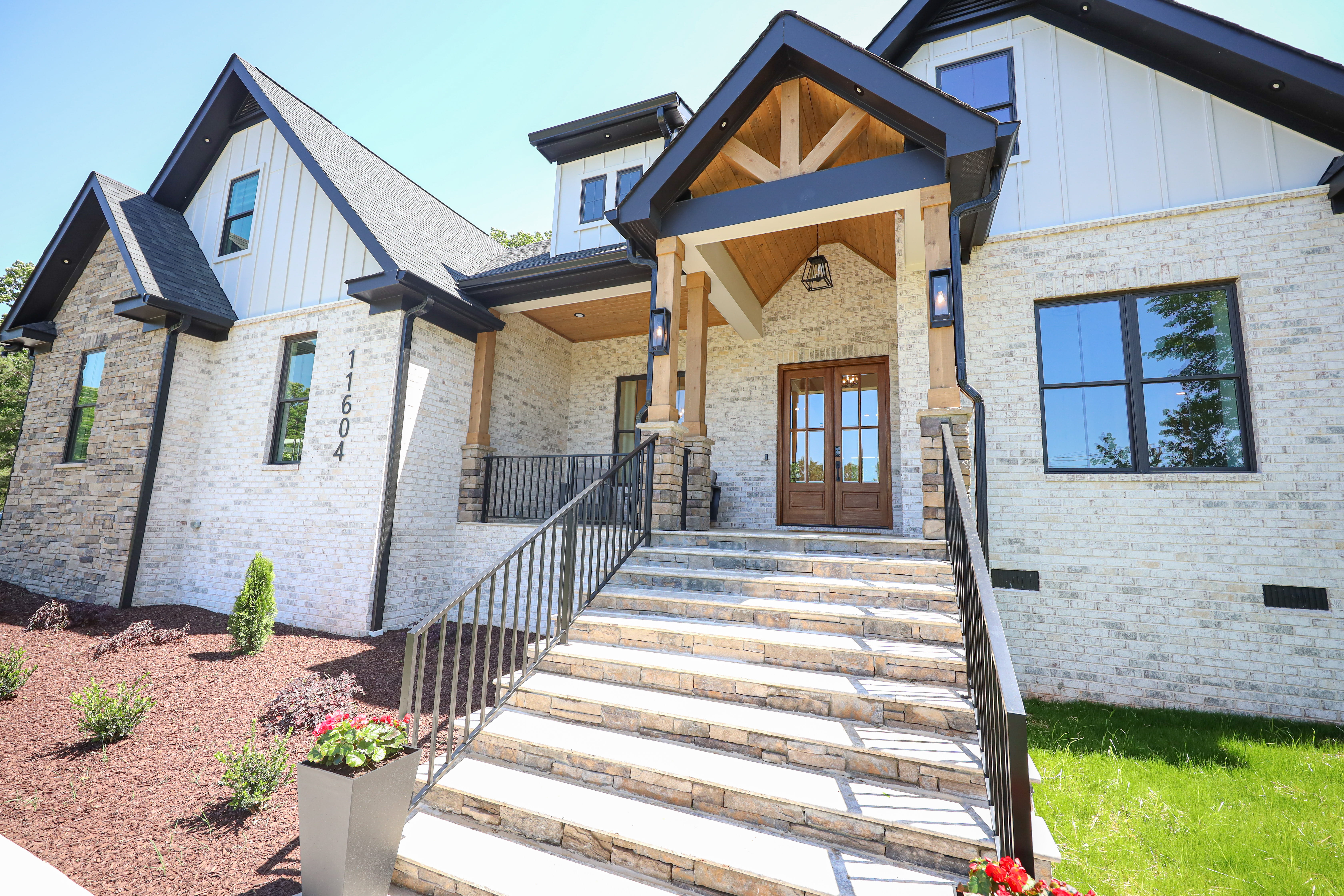Covered front entry of a custom home with white brick, stone accents, timber details, and wood double doors.