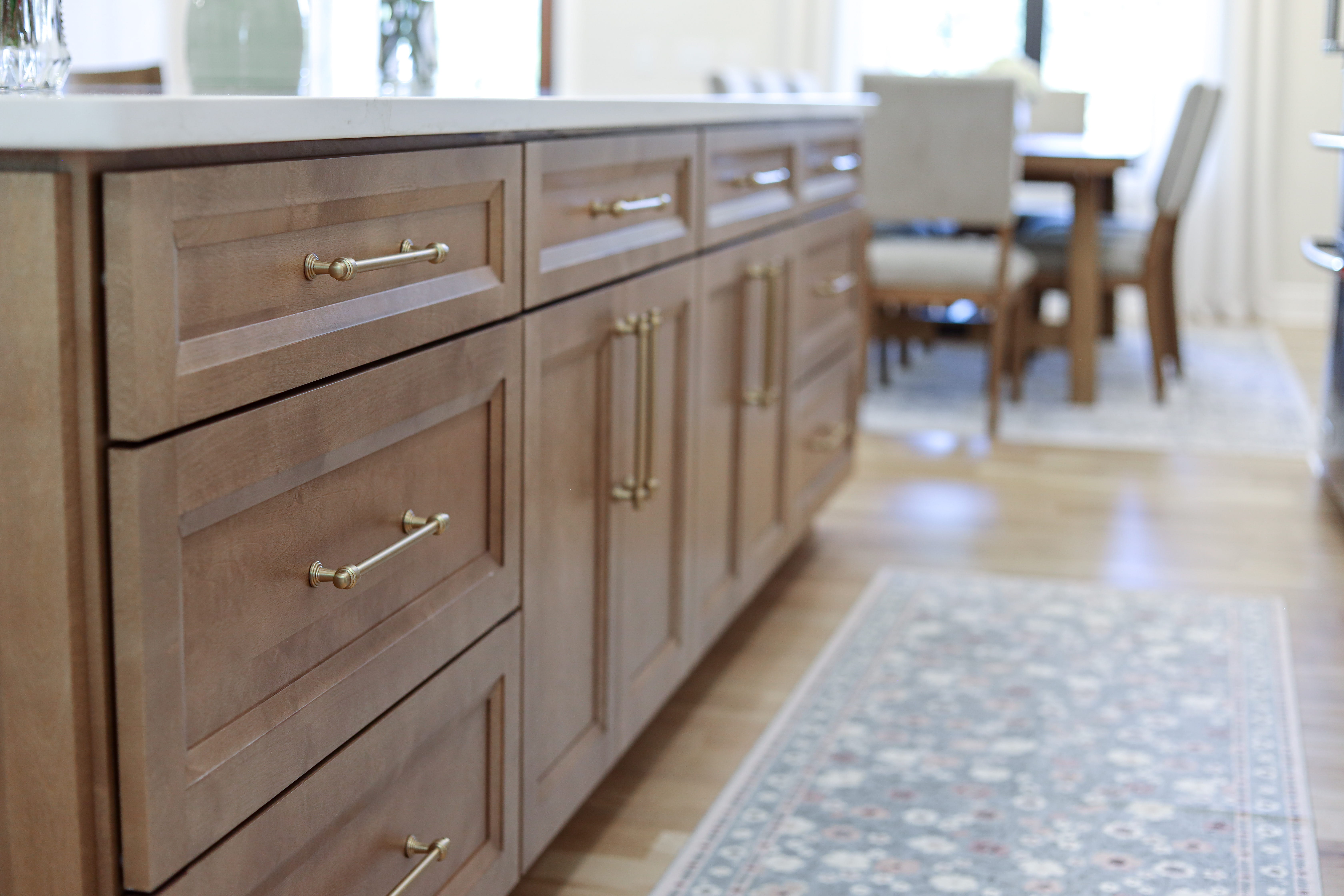 Detailed view of wood kitchen island drawers and cabinets with brass pulls beside a patterned runner rug.