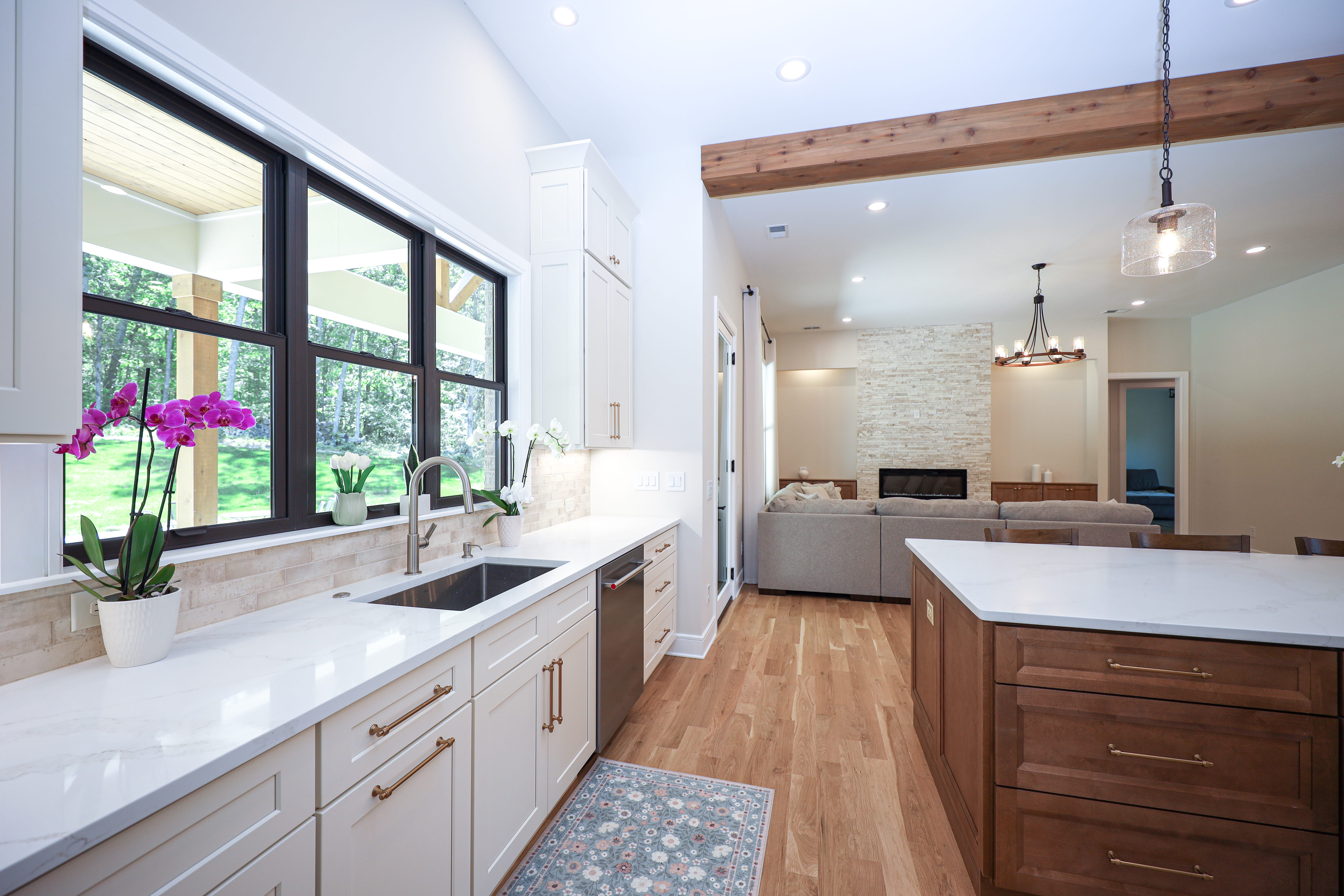 Custom kitchen sink wall with white cabinets, quartz counters, black-framed windows, orchids, and a view into the living room.