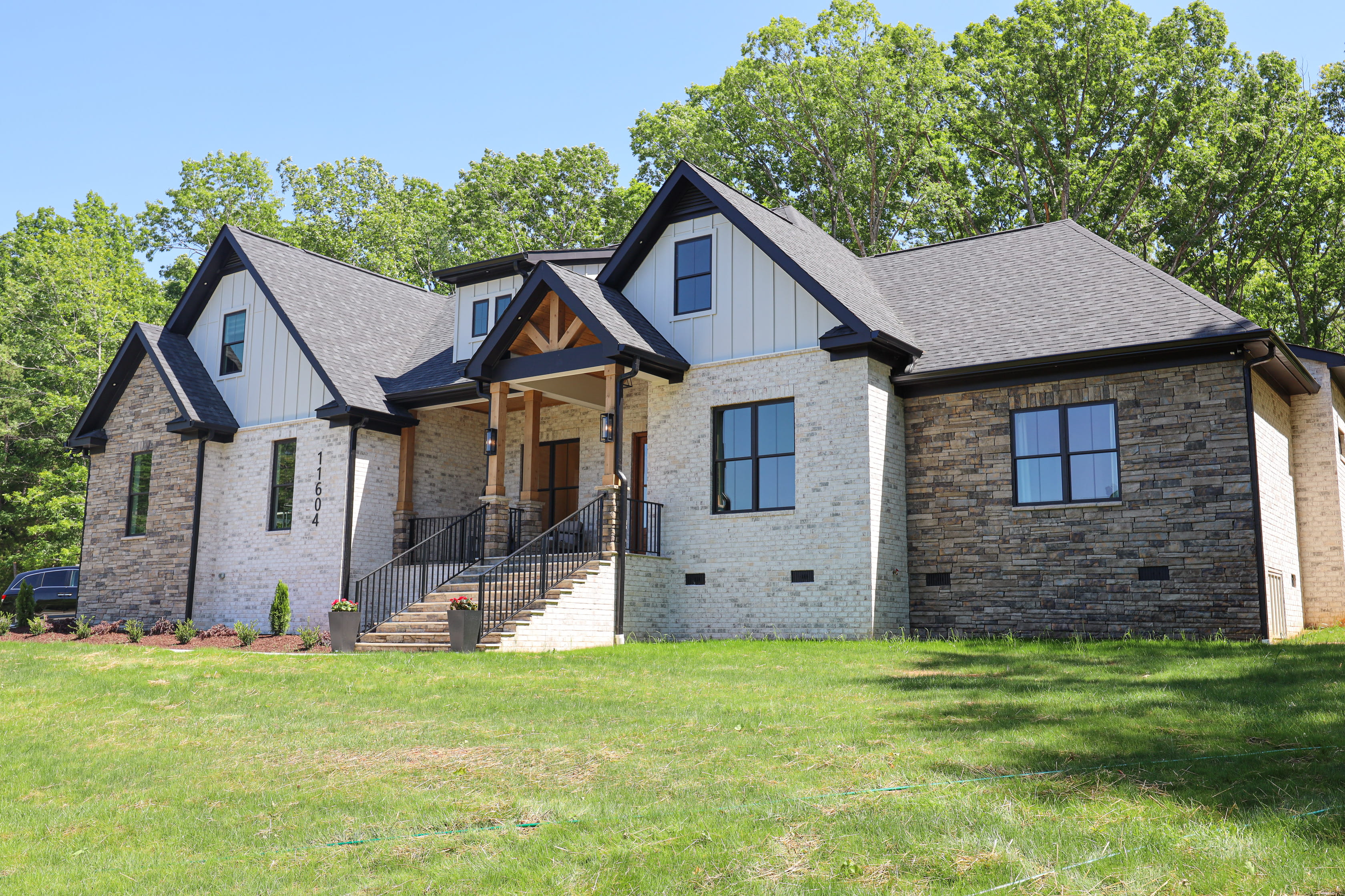 Custom home exterior with white brick, natural stone, black trim, steep gables, and a timber-framed front porch.
