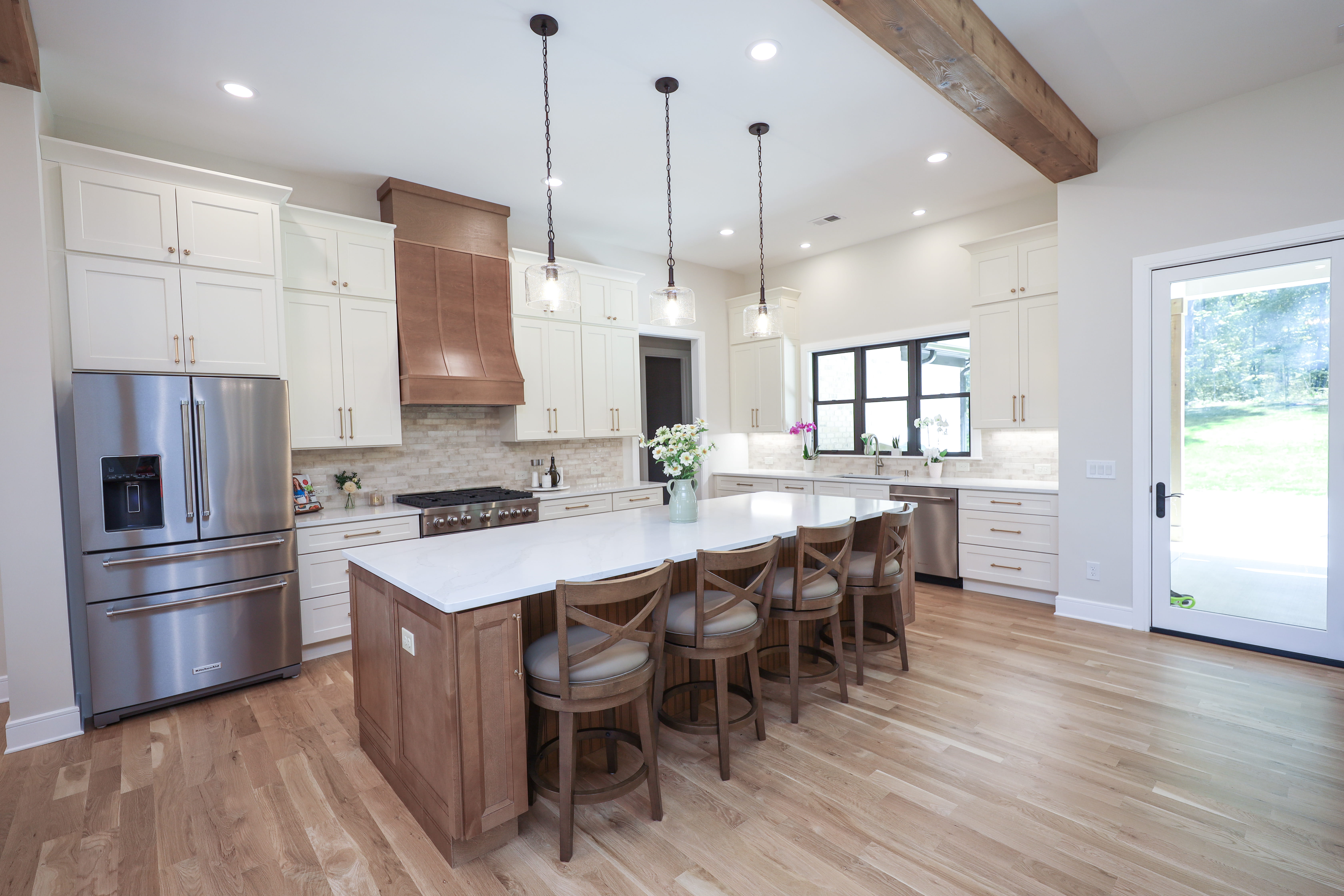Custom kitchen with white perimeter cabinets, a large wood island, quartz countertop, pendant lights, and bar seating.