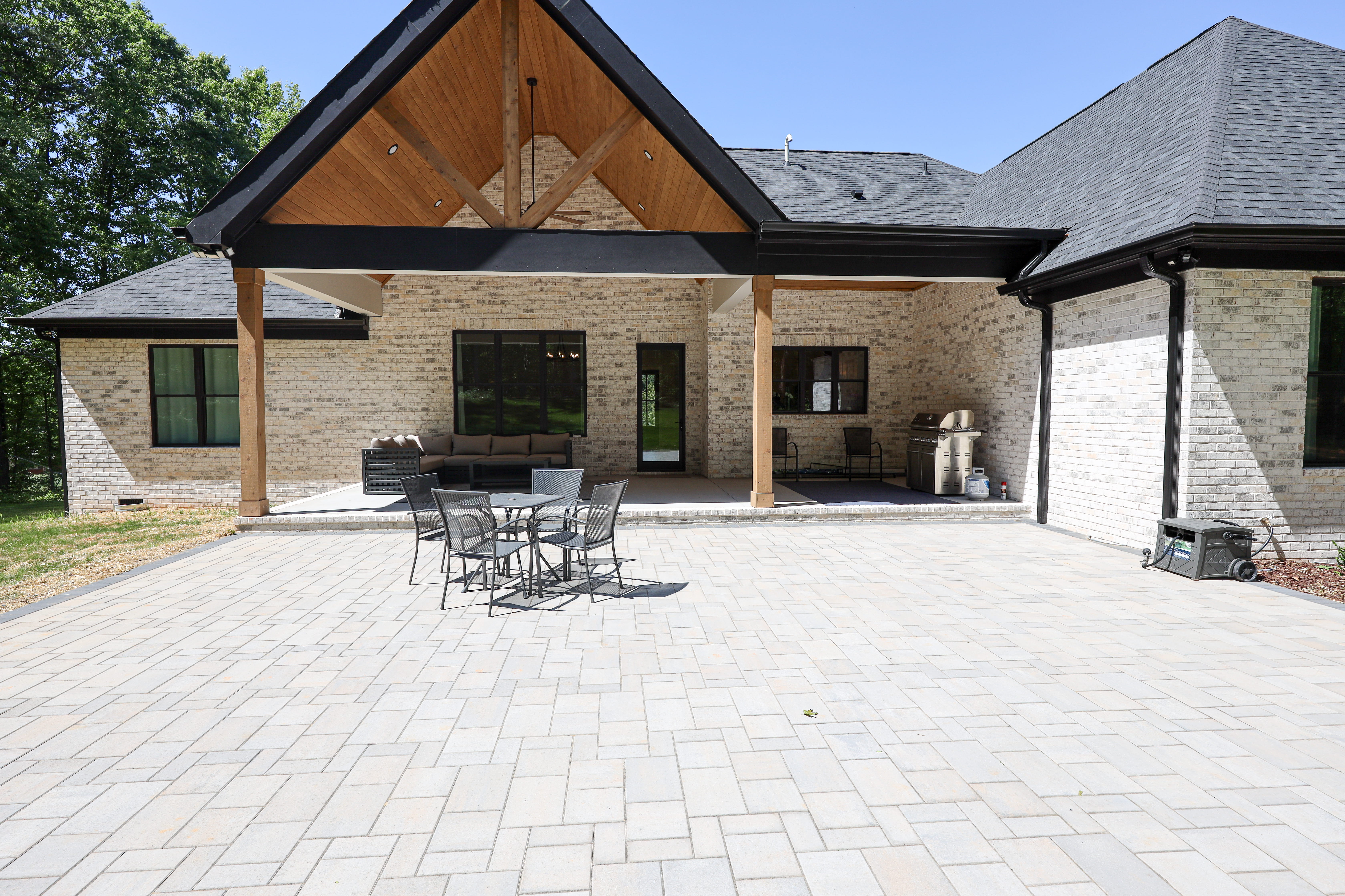 Rear exterior with a covered timber patio, white brick walls, outdoor seating, grill area, and a large paver courtyard.