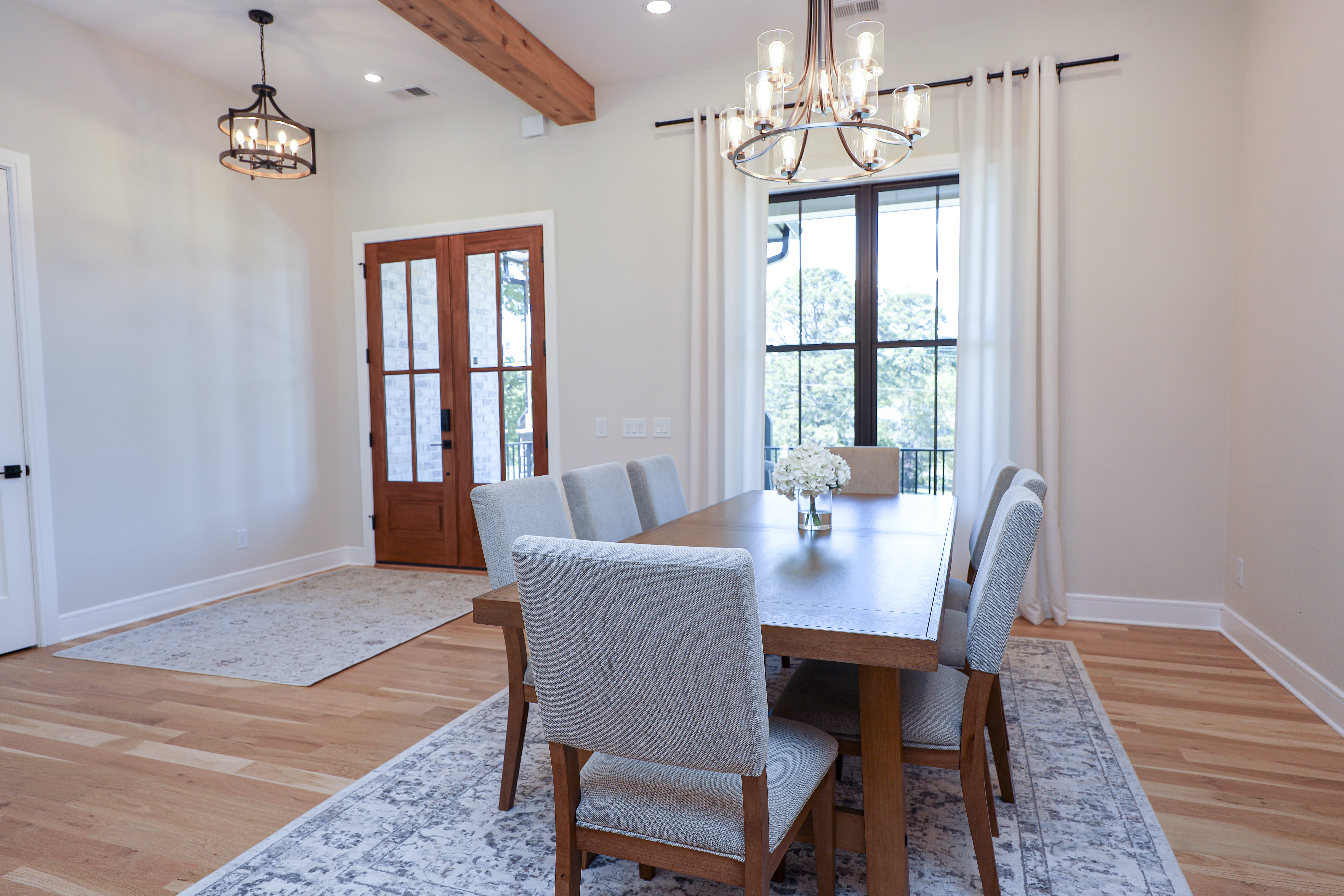 Formal dining room with a wood table, upholstered chairs, statement chandeliers, and glass-paneled wood entry doors.