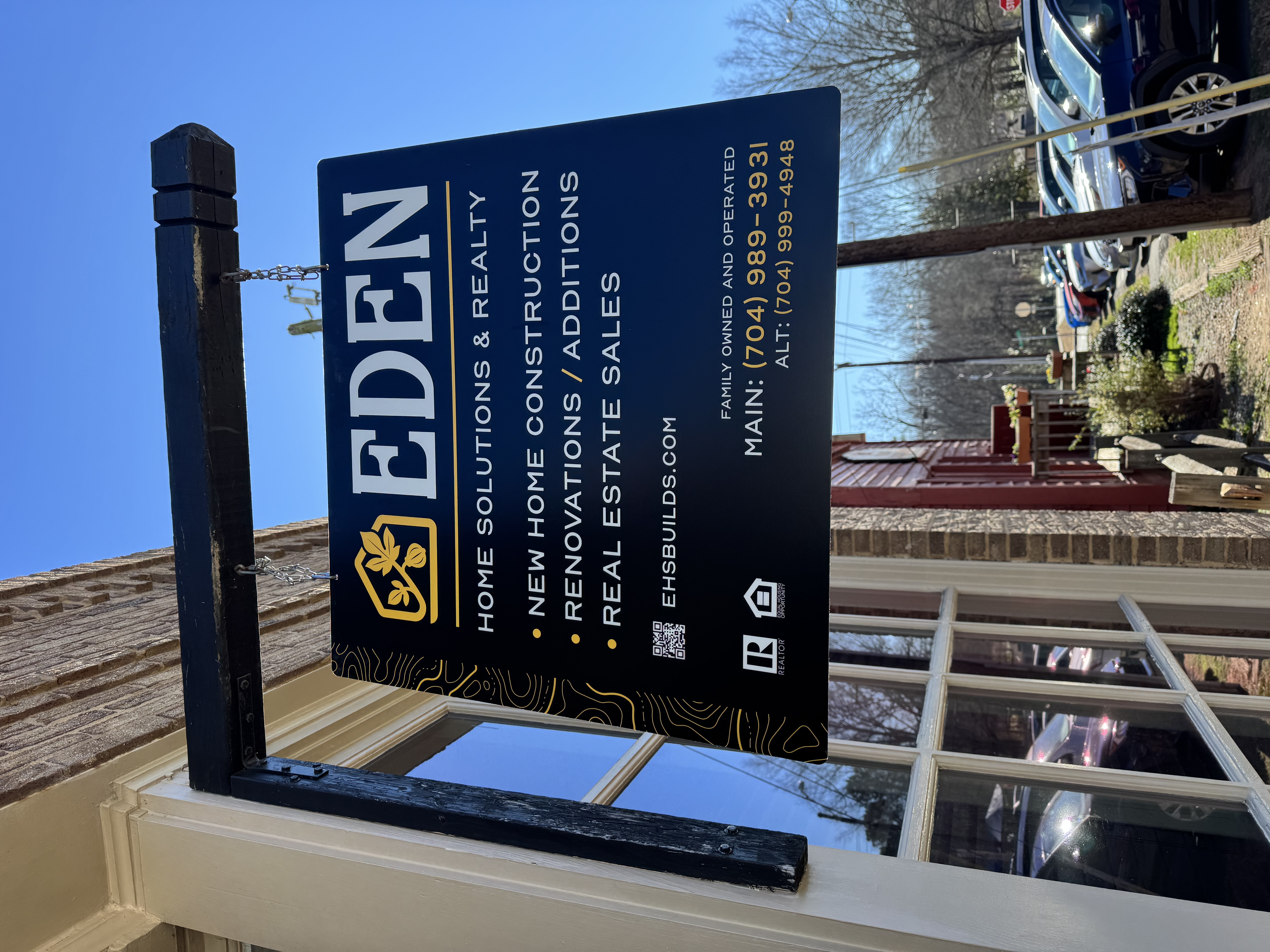 Hanging exterior sign for Eden Home Solutions & Realty displaying services and contact information.
